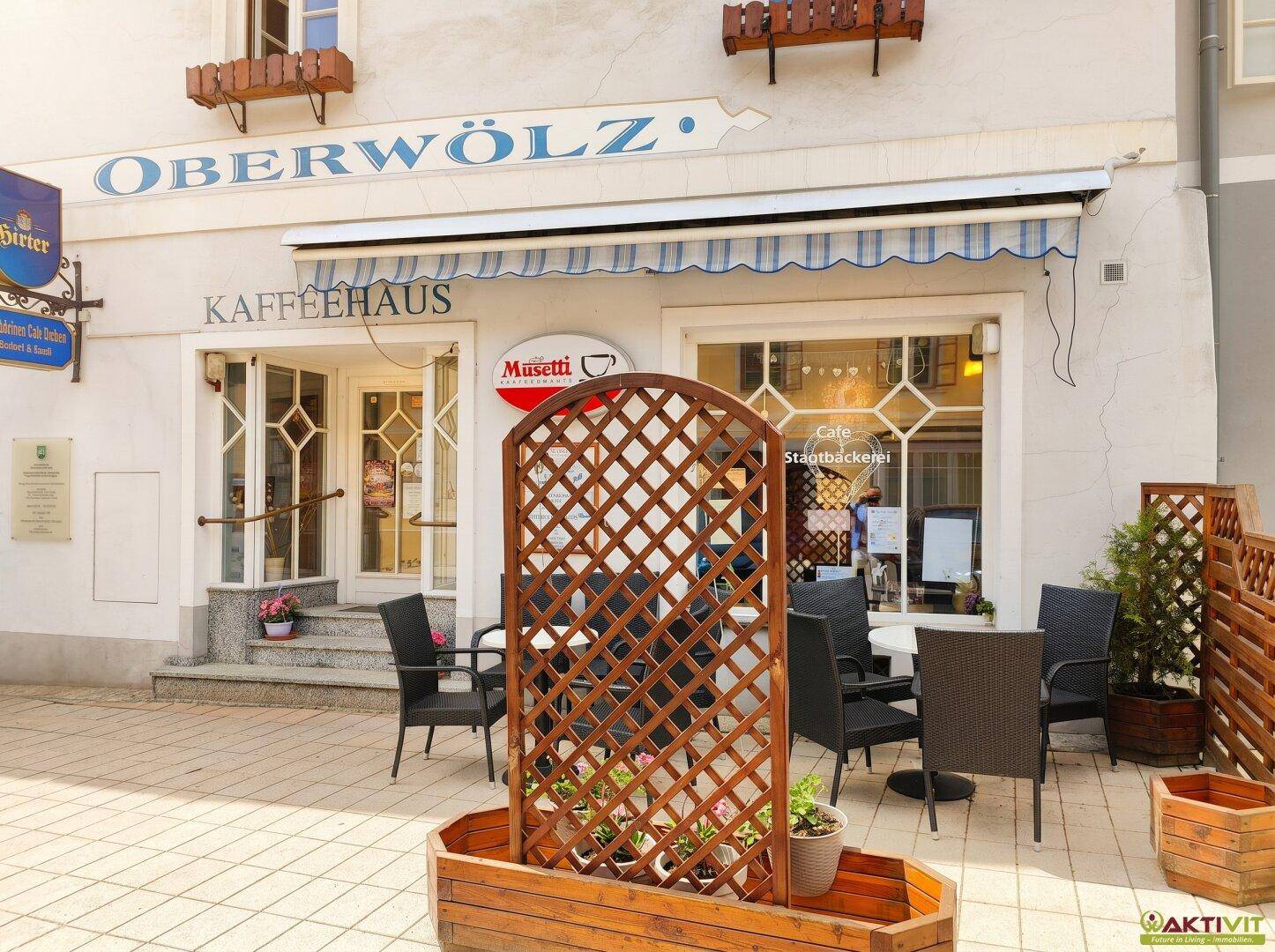 Gemütlicher Außenbereich eines Kaffeehauses mit Tischen und Stühlen auf der Terrasse.