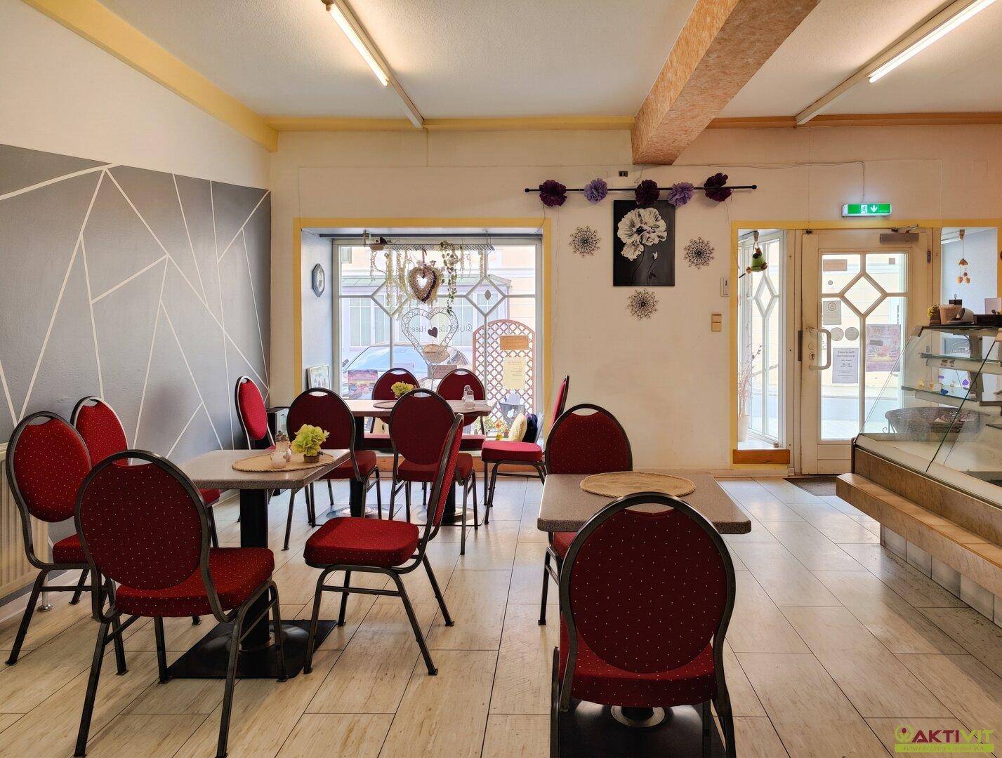Gastraum eines Cafés mit roten Stühlen, Tischen und modernem Wanddesign.