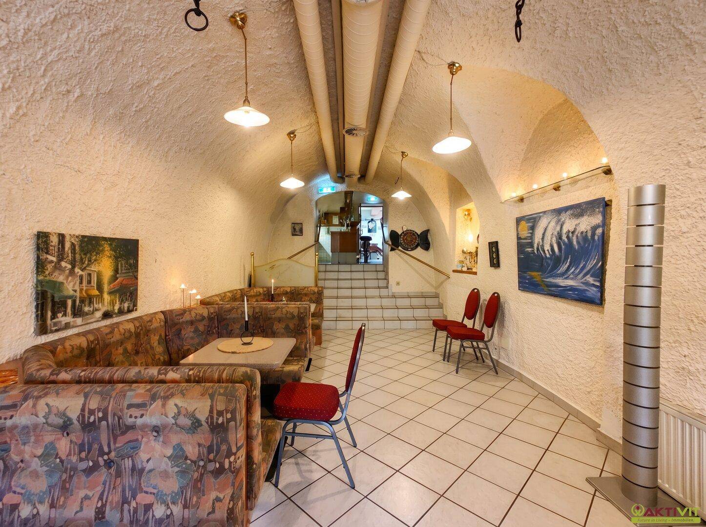 Langer Gastraum mit gewölbter Decke, Sitzbänken und Kunstwerken an den Wänden.