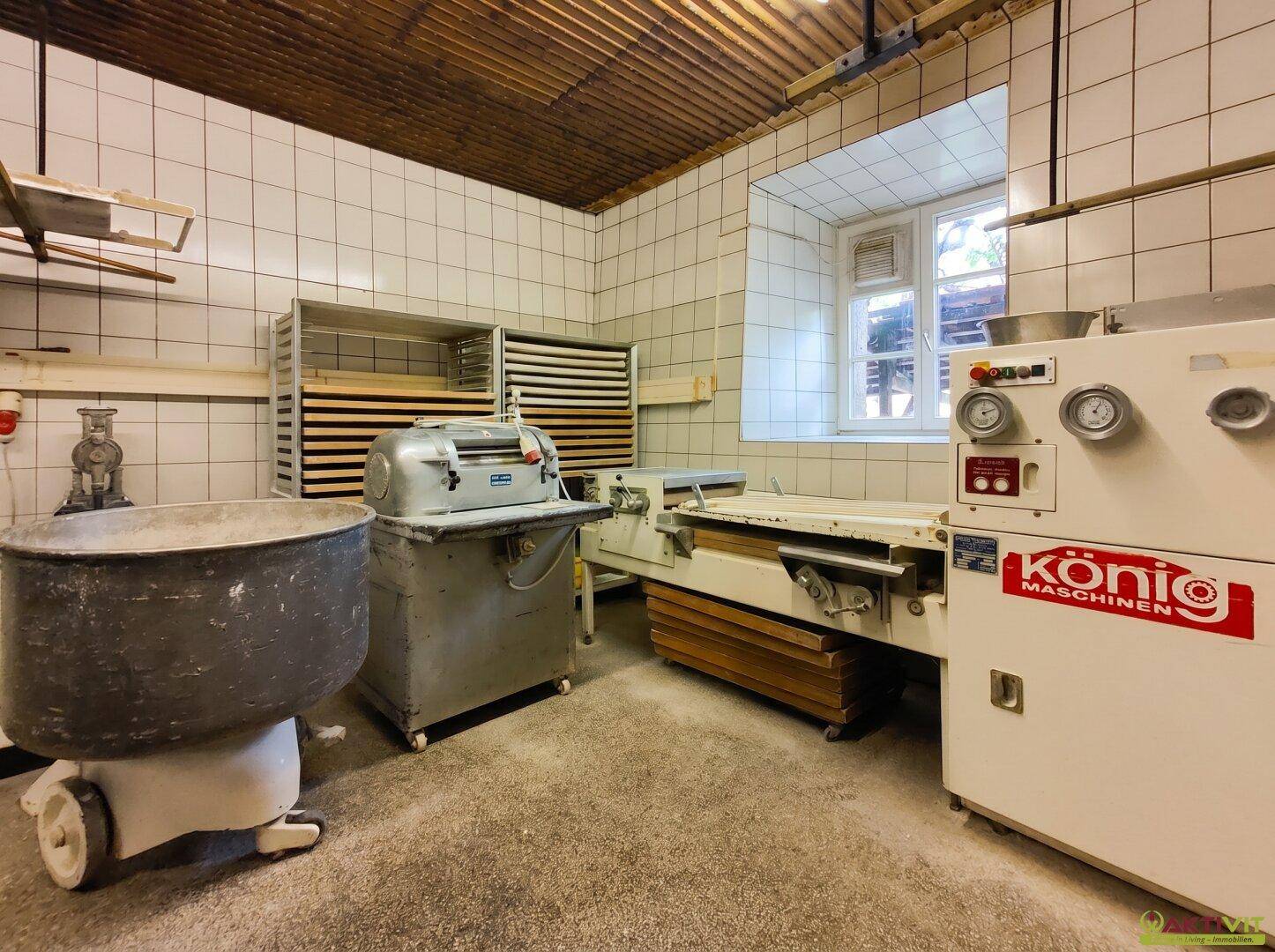 Bäckereiproduktionsraum mit großen Maschinen, gefliesten Wänden und Fenster.