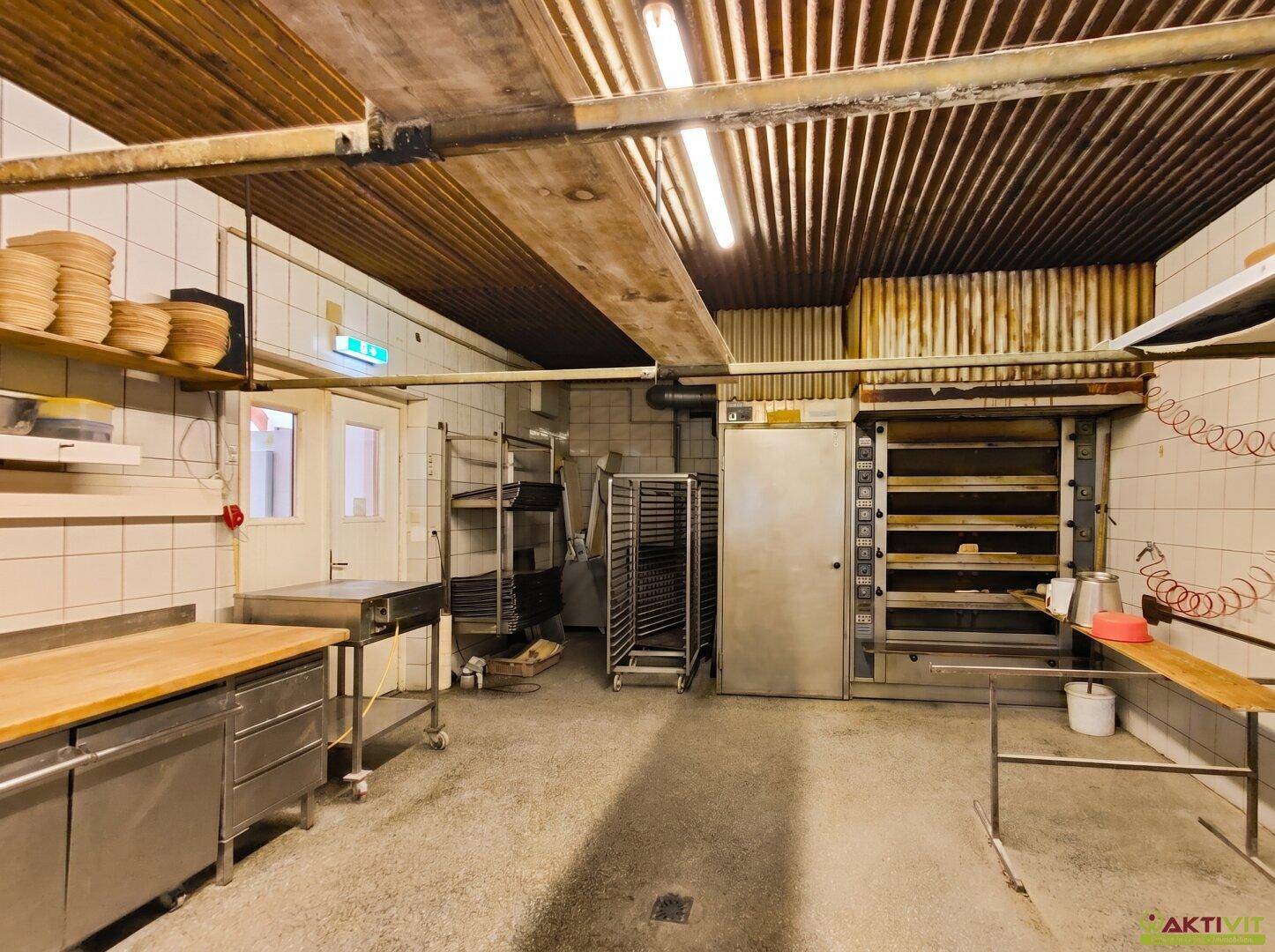 Bäckereiproduktionsraum mit großen Öfen, Regalen und einer Holzdecke.