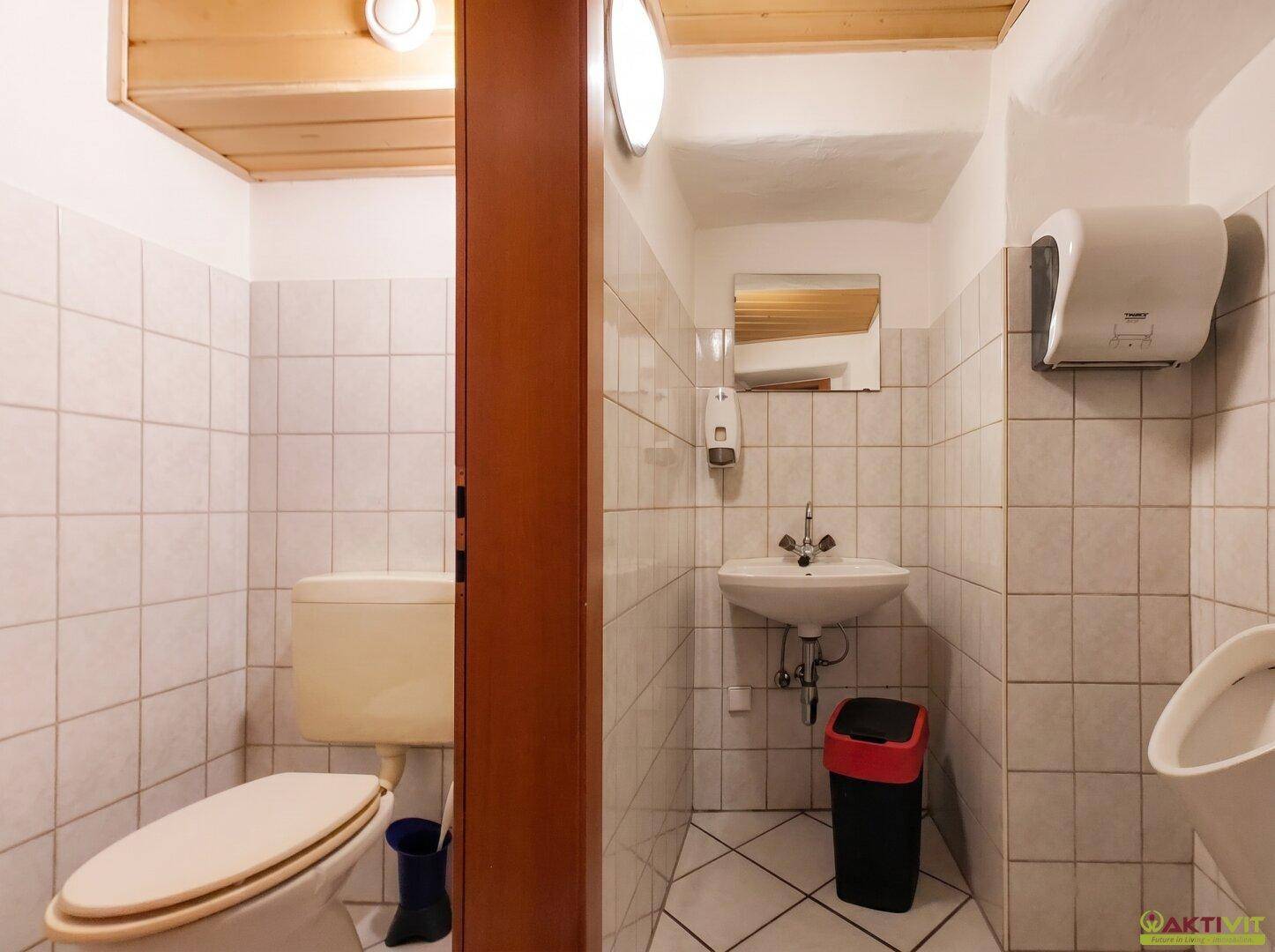 Gefliester Toilettenraum mit WC, Waschbecken und Urinal in einem öffentlichen Bereich.