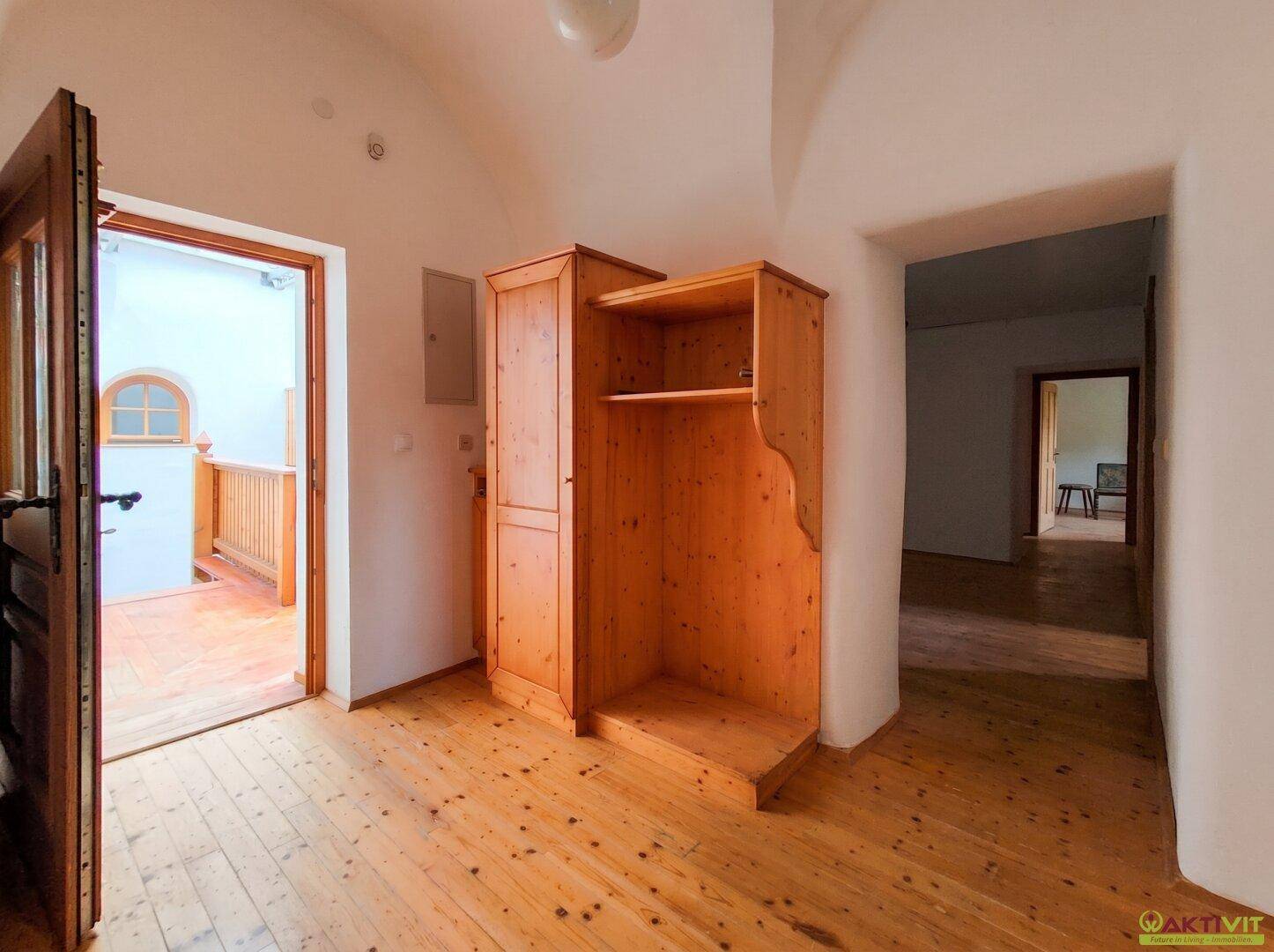 Zimmer mit Holzboden, Holzschrank und gewölbter Türöffnung zu einem weiteren Bereich.