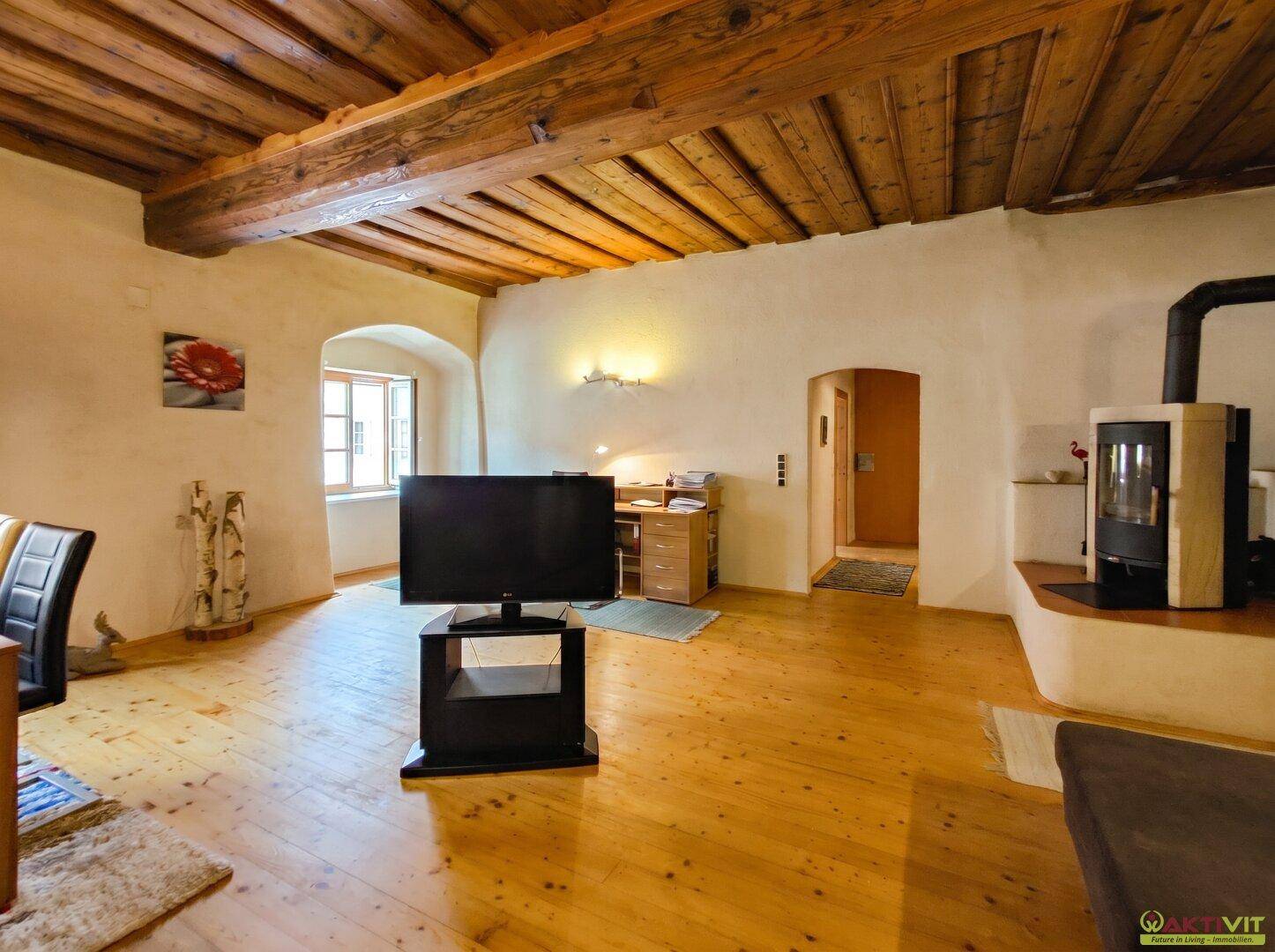 Helles Wohnzimmer mit Holzbalkendecke, Holzboden und modernem Holzofen.
