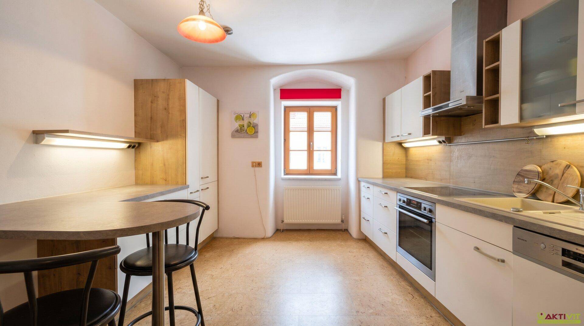 Moderne Küche mit weißen Schränken, Holzelementen, integriertem Essbereich und einem Fenster.