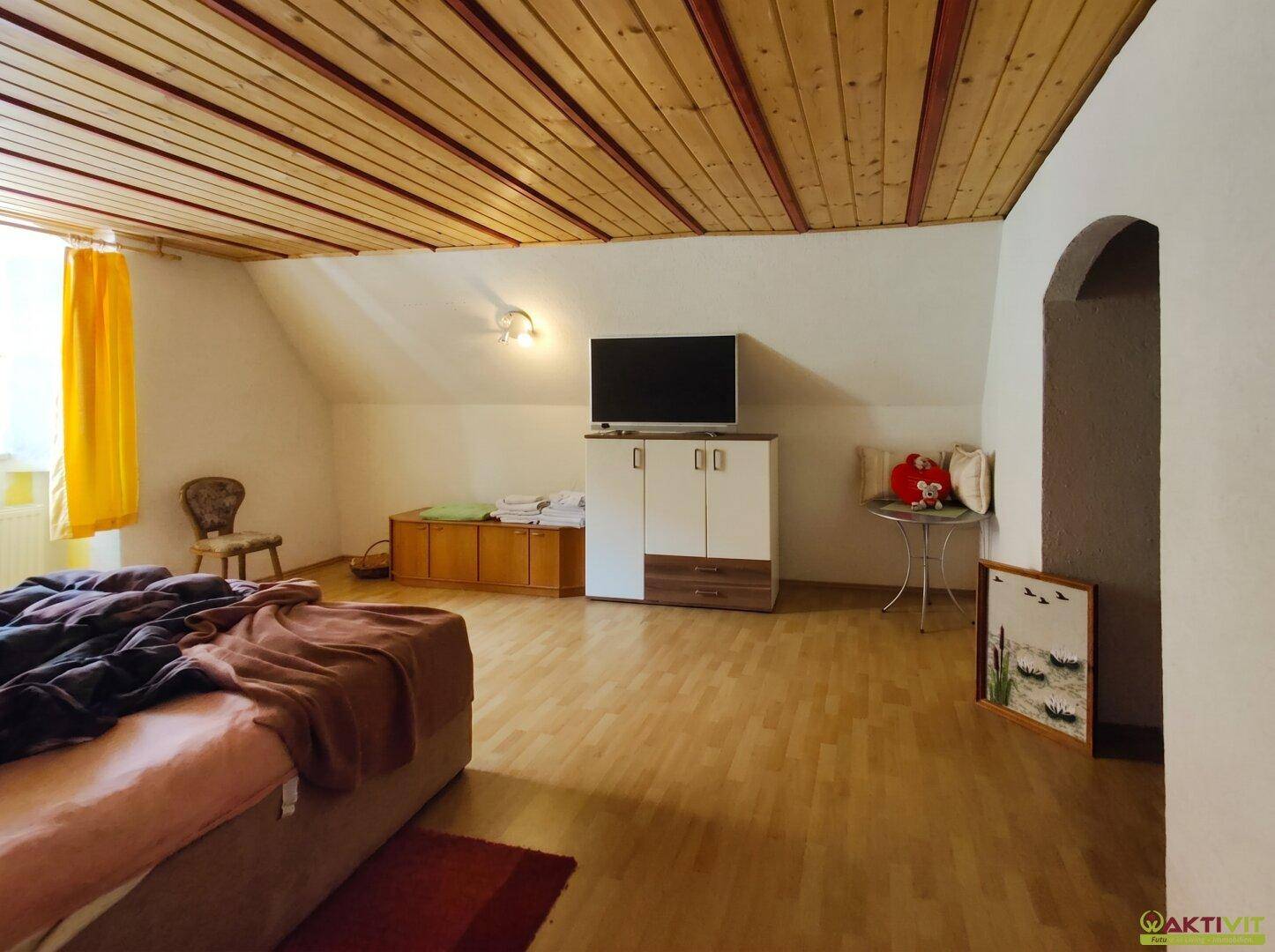 Gemütliches Schlafzimmer mit Holzbalkendecke, Holzboden und einem Fenster.