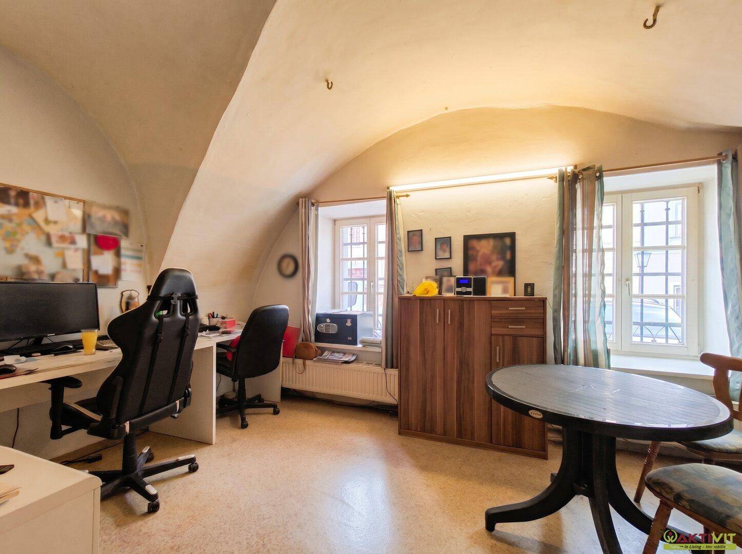 Arbeitszimmer mit gewölbter Decke, zwei Fenstern, Schreibtischen und einem Holzkabinett.