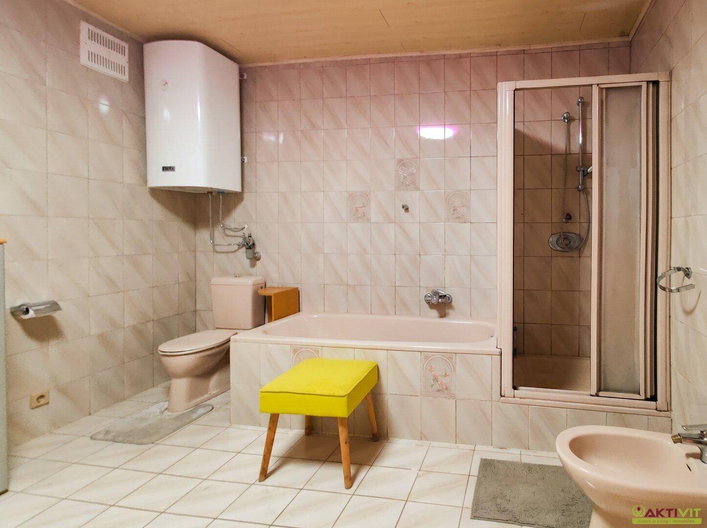 Gefliestes Badezimmer mit Badewanne, Duschkabine, Toilette und Bidet in Pastellfarben.