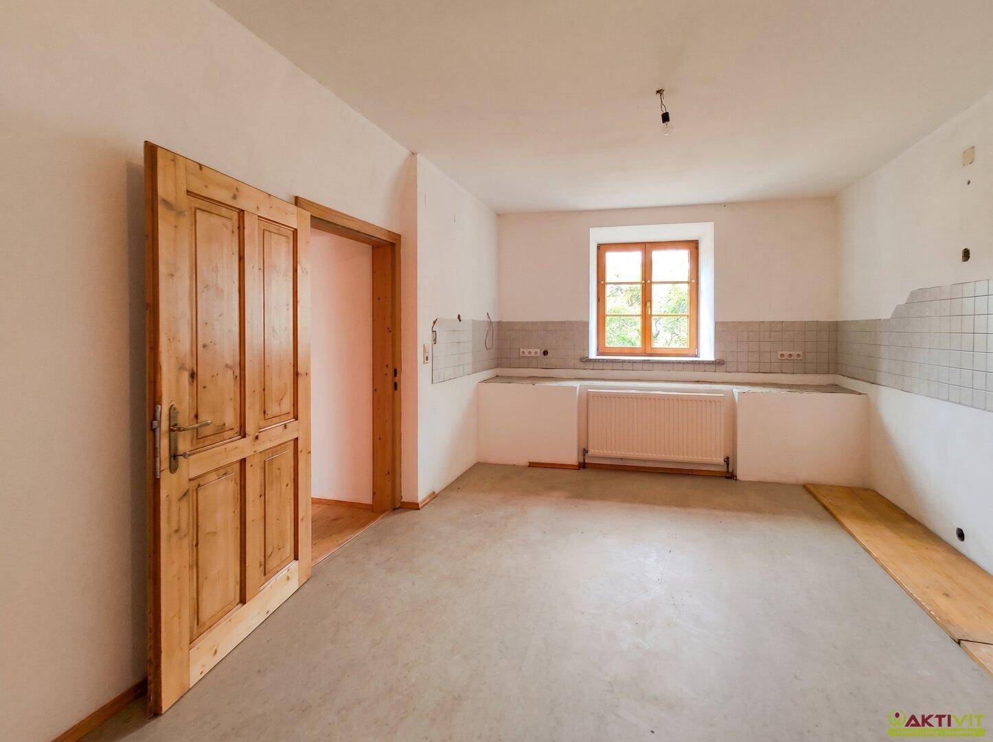 Leerer Küchenraum mit Fliesenrückwand, Fenster und Holztür, bereit für die Einrichtung.