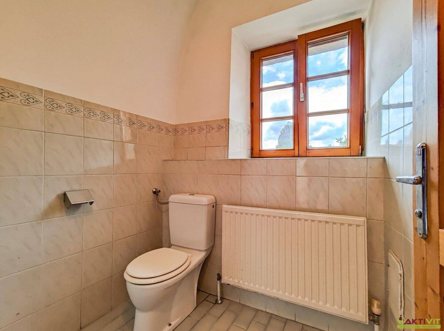 Geflieste Toilette mit Fenster und Heizkörper.