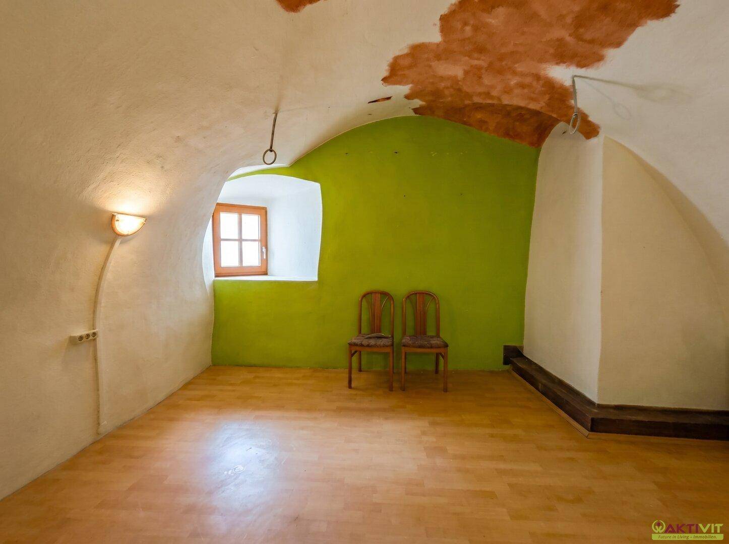 Heller Raum mit gewölbter Decke, grüner Akzentwand und Holzboden.