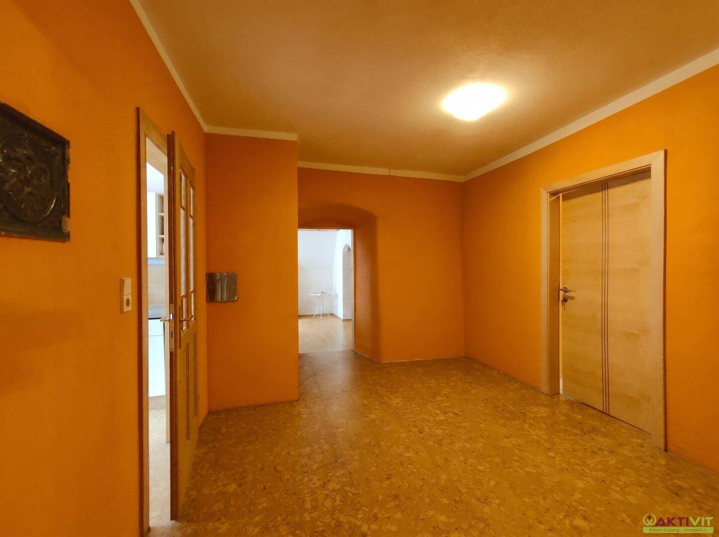 Langer Flur mit orangefarbenen Wänden, Fliesenboden und Holztüren.