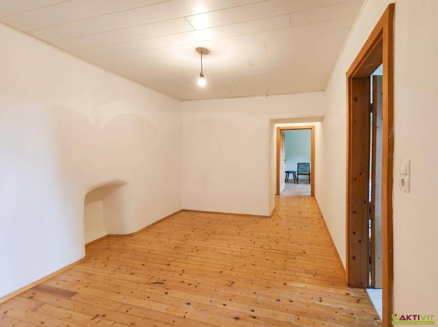 Helles, leeres Zimmer mit Holzboden und weiß gestrichenen Wänden.
