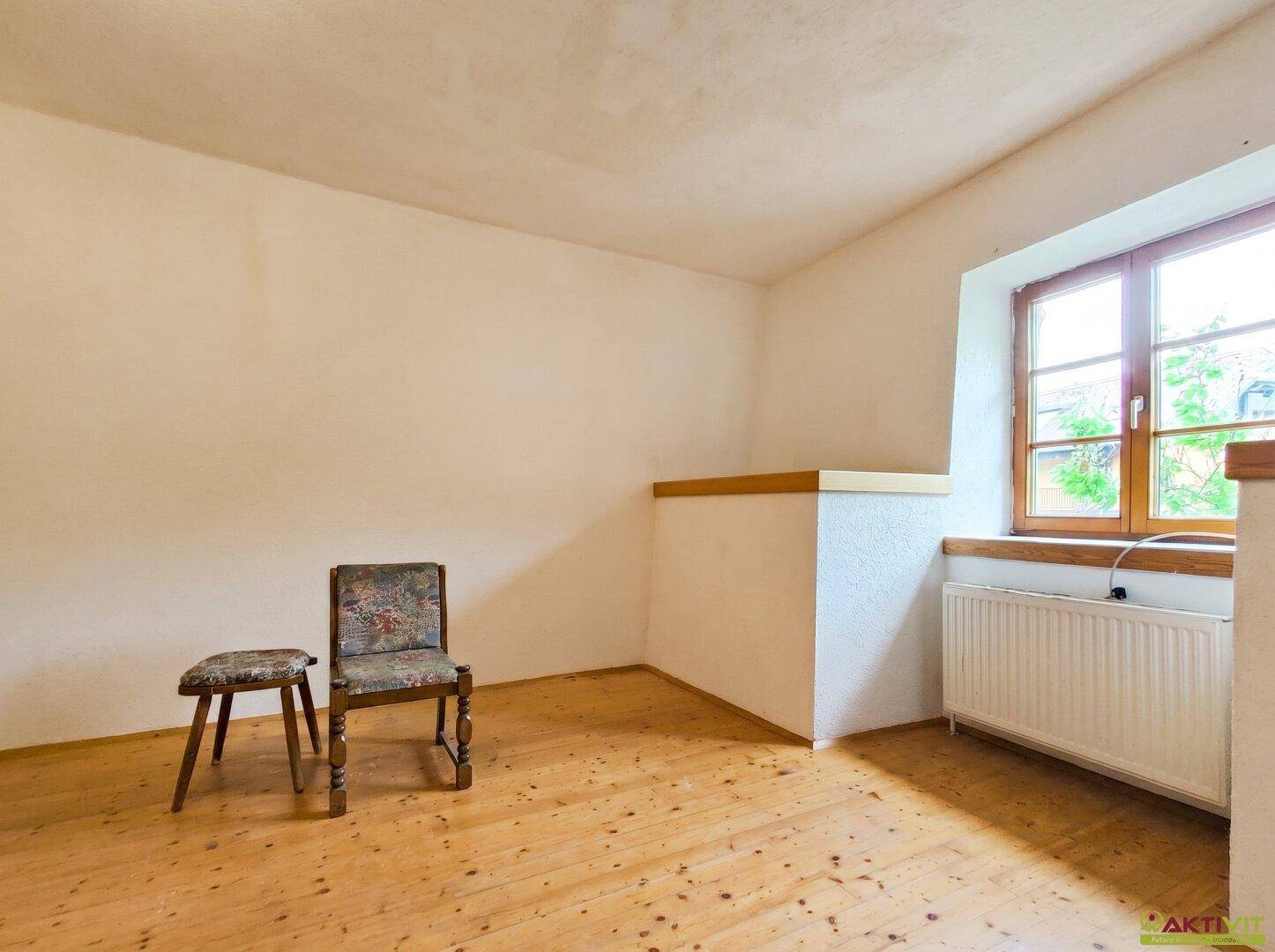 Leeres Zimmer mit Holzboden, Fenster und Heizkörper.