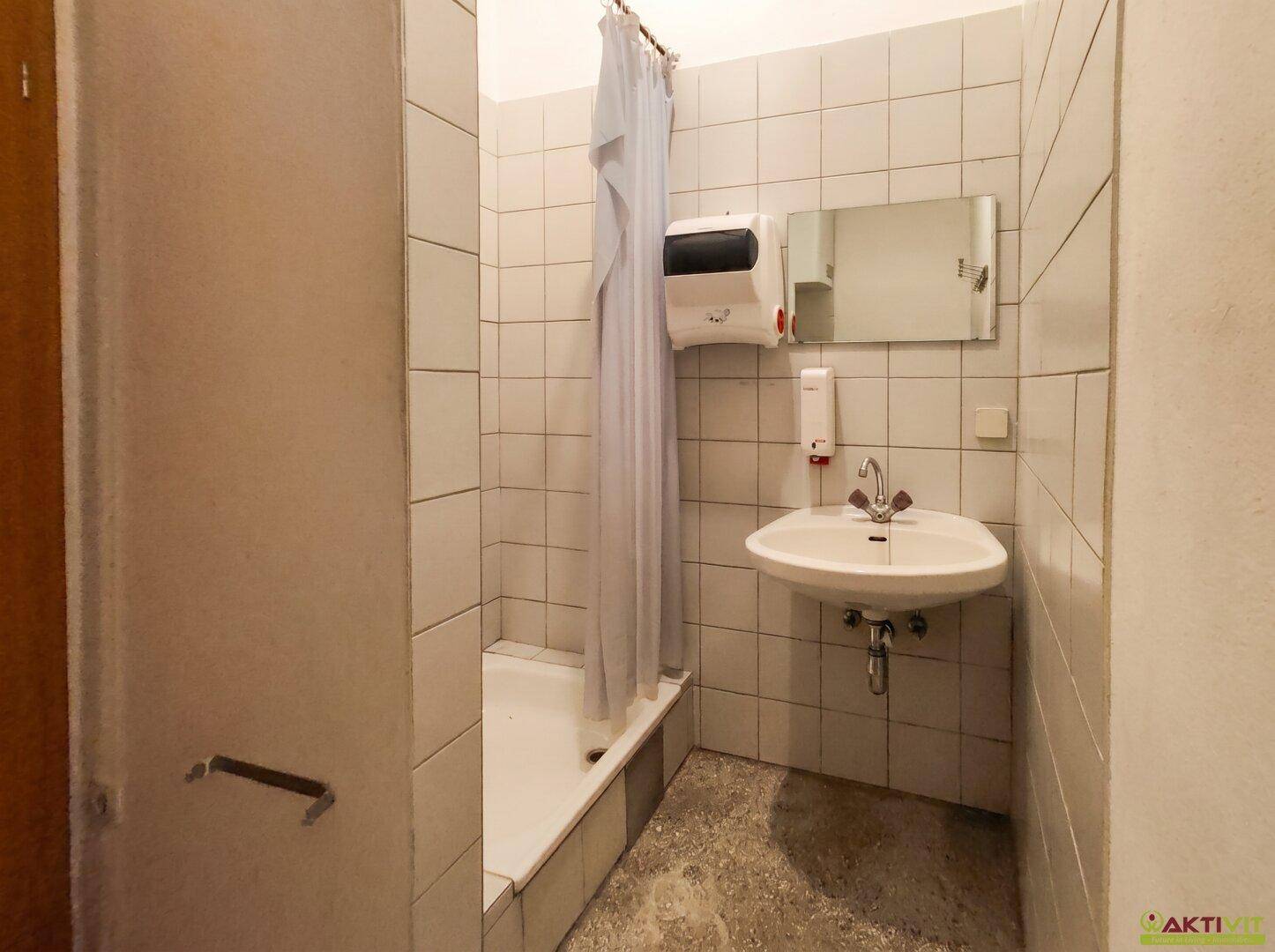 Kleines Badezimmer mit Duschbereich, Waschbecken und Spiegel.