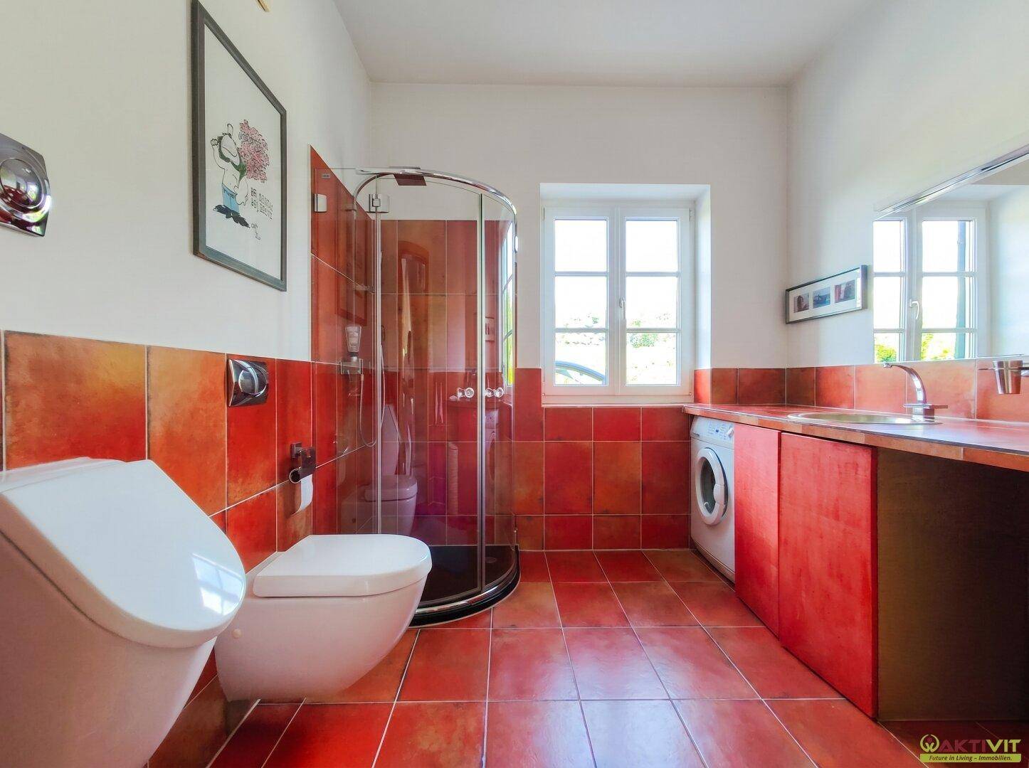 Modernes Badezimmer mit roten Fliesen, Dusche, WC und Waschmaschinenanschluss.
