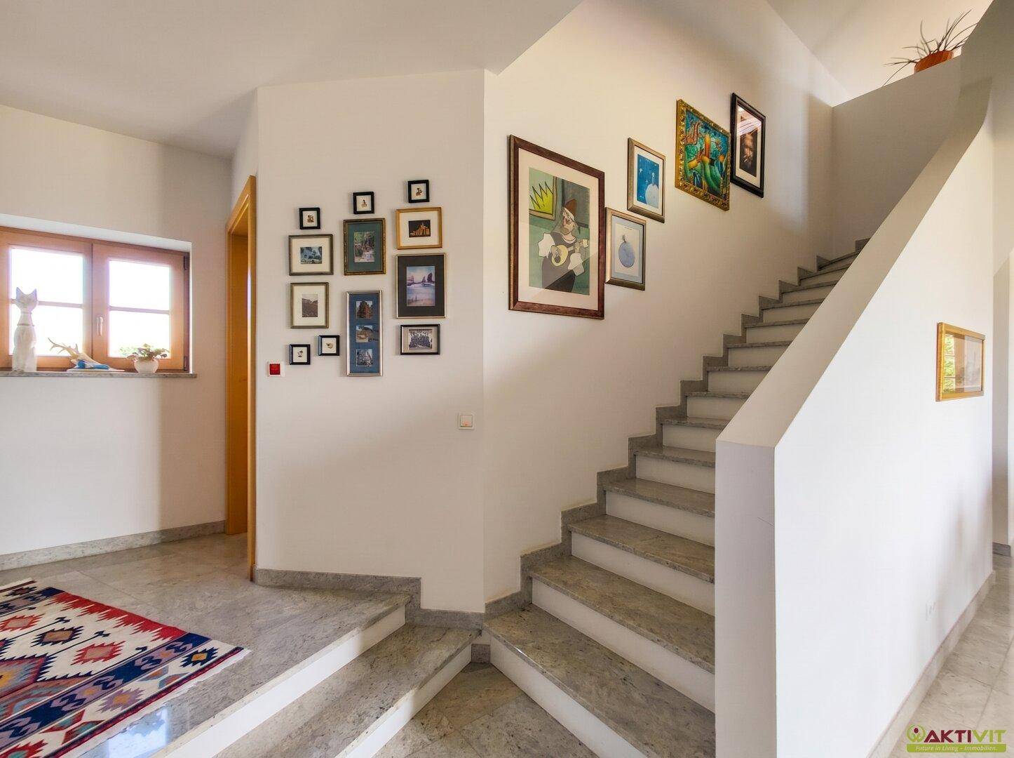 Heller Flur mit eleganter Treppe, glänzendem Marmorboden und dekorativen Bildern.