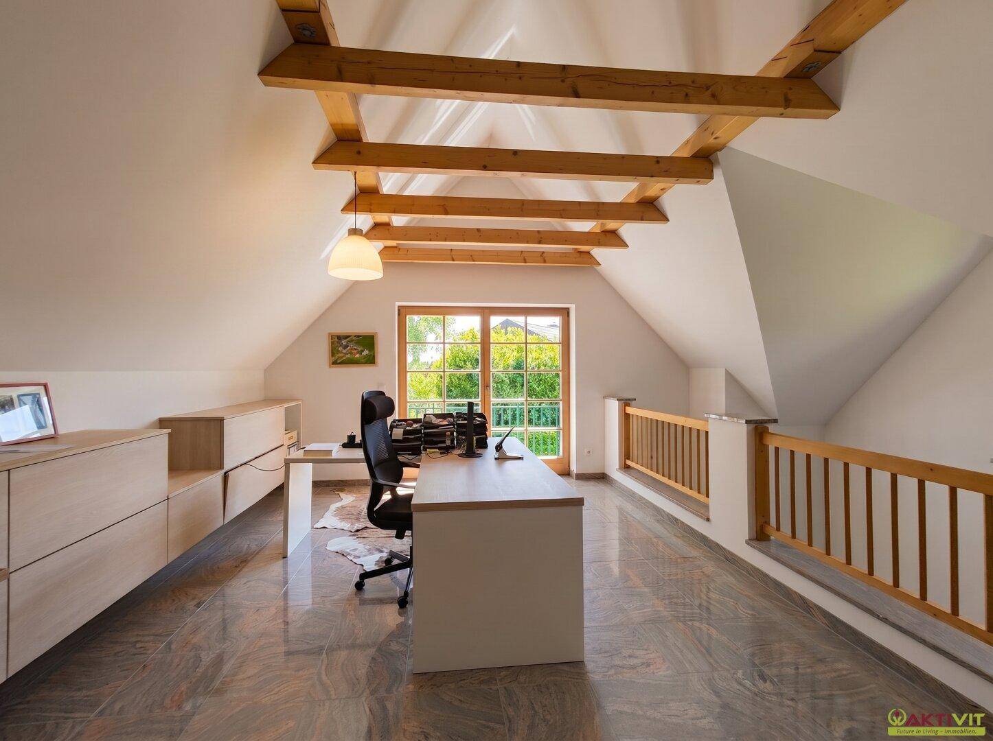 Helles Dachgeschoss-Büro mit sichtbaren Holzbalken, großem Fenster und weitem Ausblick.