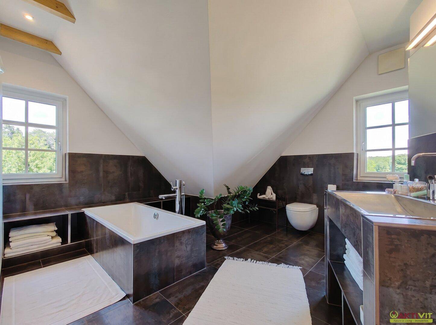 Modernes Badezimmer im Dachgeschoss mit Badewanne, Doppelwaschbecken und Fensterblick.