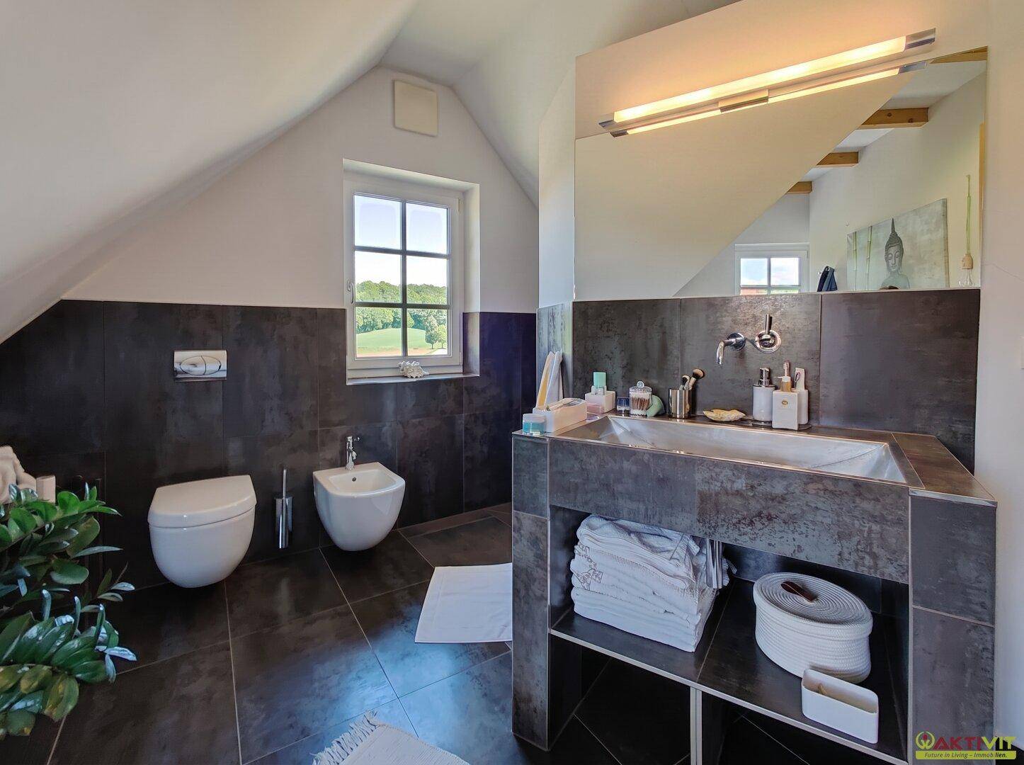 Elegantes Badezimmer mit großem Spiegel, Bidet und Fenster mit Blick ins Grüne.