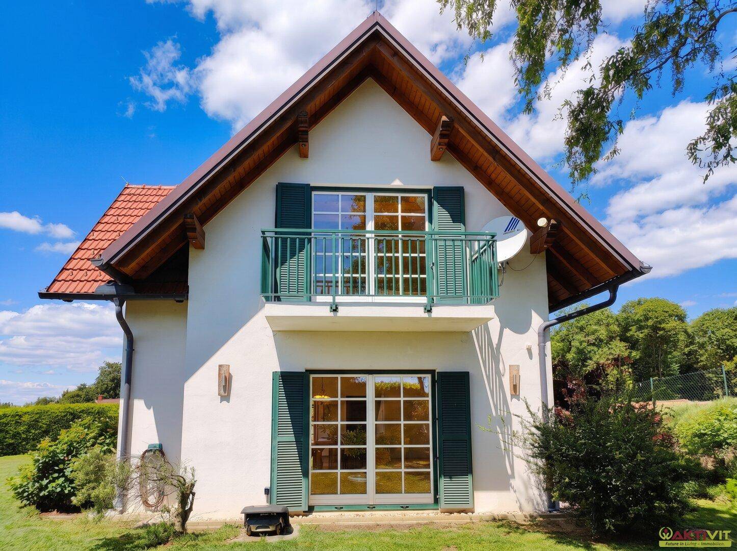 Seitenansicht des Hauses mit Balkon, großen Fenstern und grünen Fensterläden.