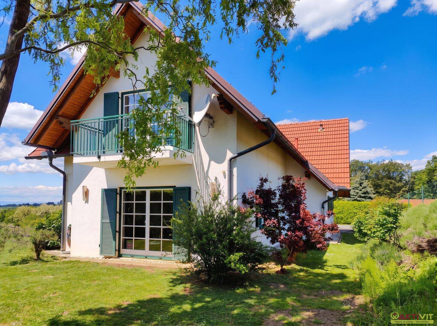 Charmante Seitenansicht des Hauses mit Balkon und umgebender grüner Landschaft.