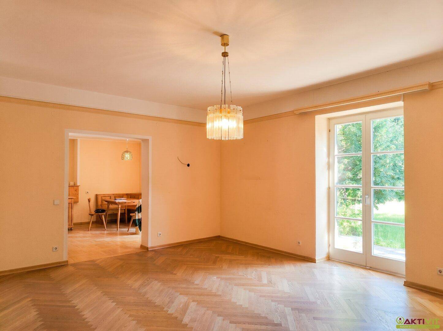 Wohnzimmer mit Fischgrätparkett und Durchgang zu einem Essbereich mit Holztisch.