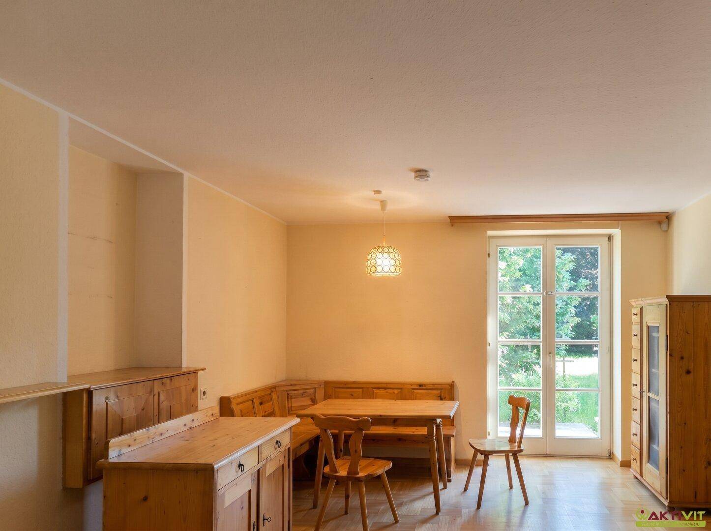 Gemütlicher Essbereich mit Holztisch, Eckbank und Blick in den grünen Garten.