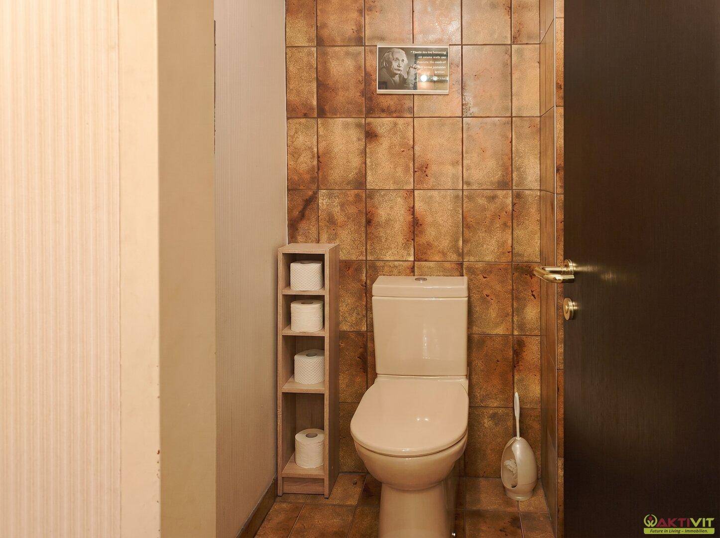 Separate Toilette mit braunen Fliesen, WC und kleinem Regal für Toilettenpapier.