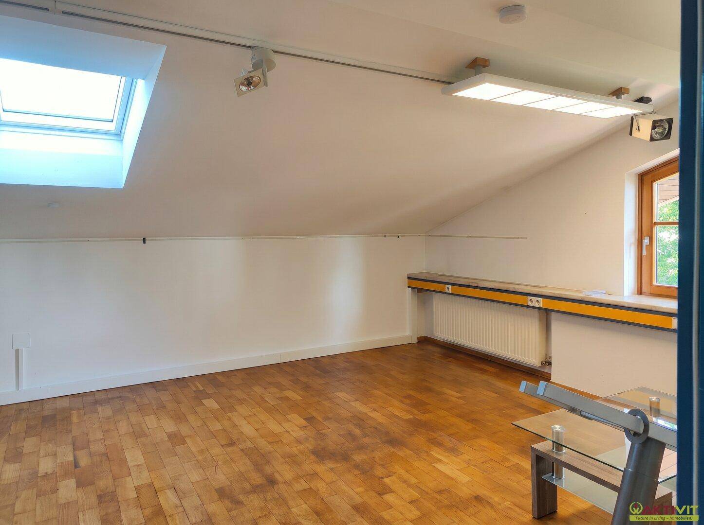 Dachgeschossraum mit Holzboden, Dachfenster und schrägen Wänden.
