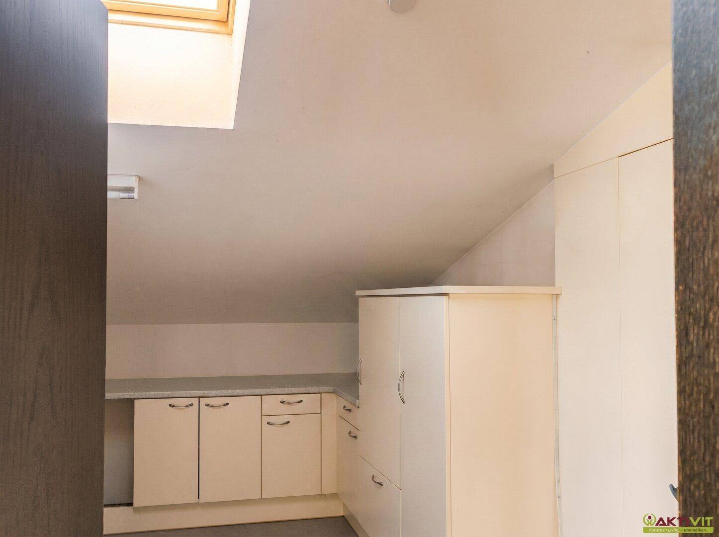 Dachgeschossküche mit weißen Einbauschränken, Arbeitsplatte und Dachfenster.