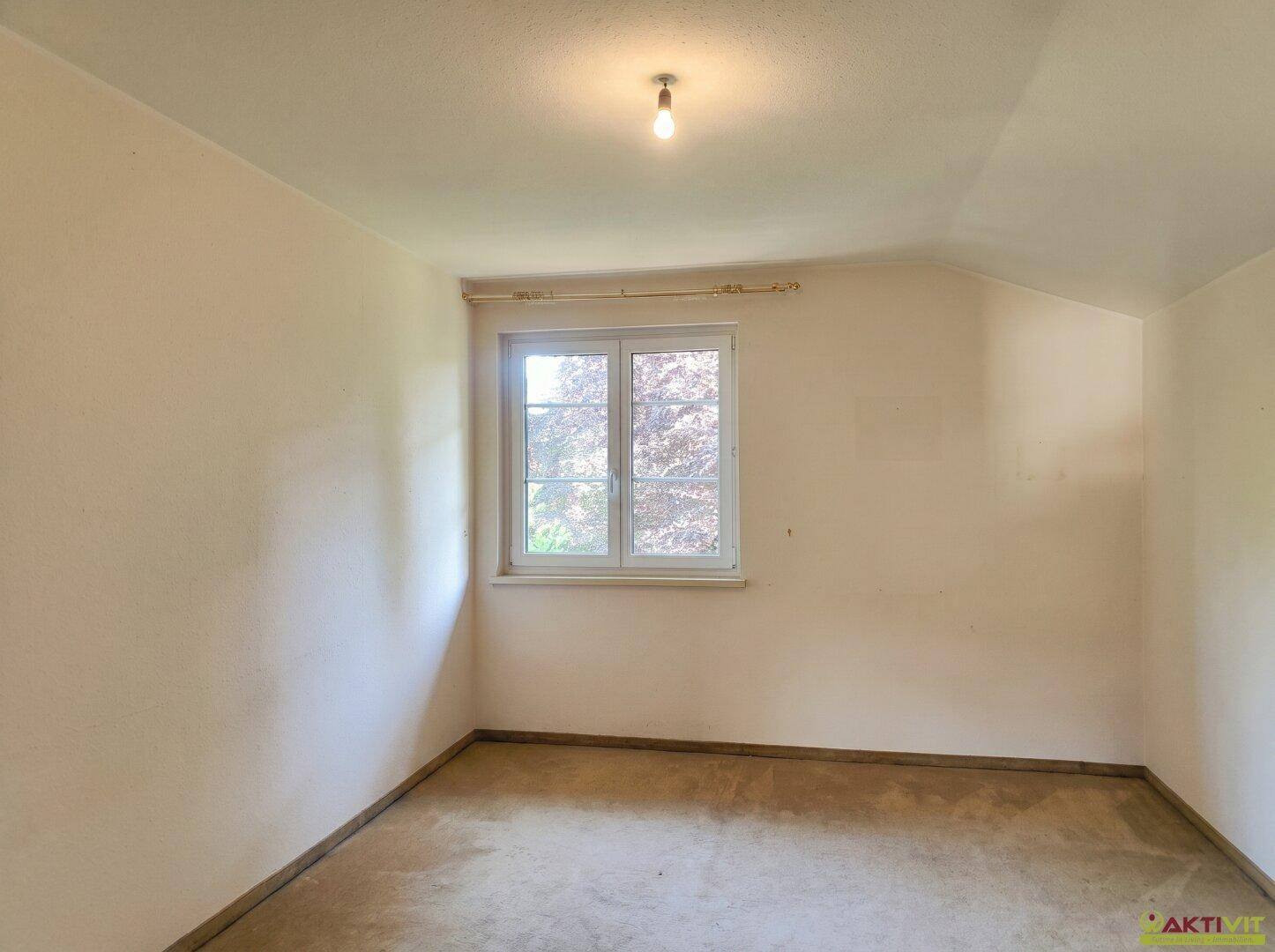 Schlafzimmer mit Teppichboden, Fenster und schlichten, hellen Wänden.