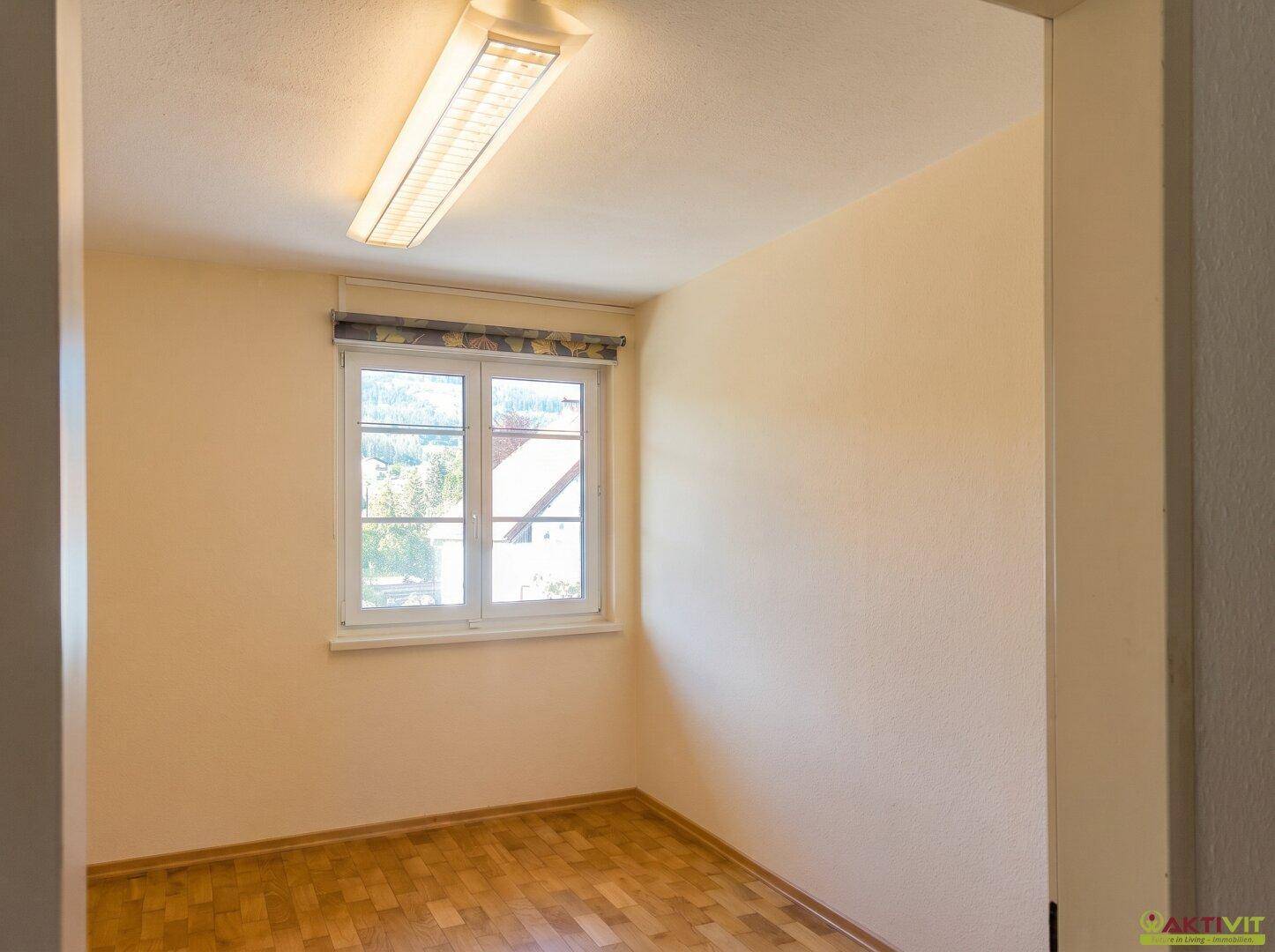 Helles Schlafzimmer mit Holzboden und Fenster, das viel Tageslicht hereinlässt.