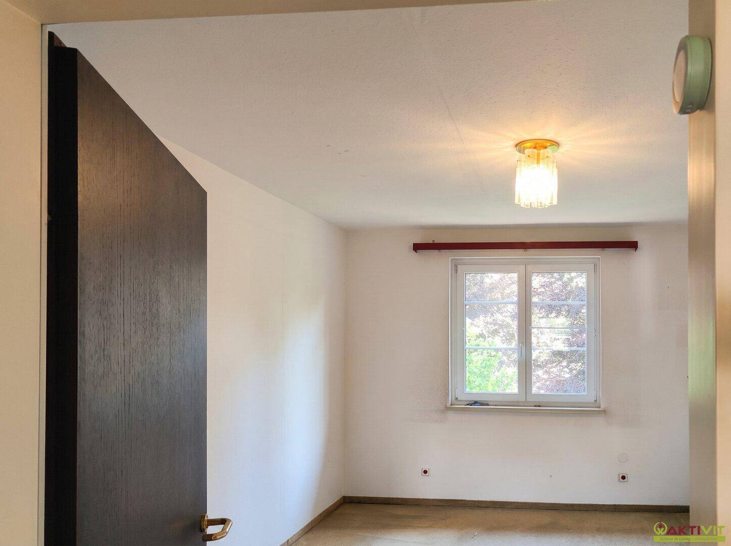 Schlafzimmer mit Teppichboden und Fenster, das einen Blick ins Grüne bietet.