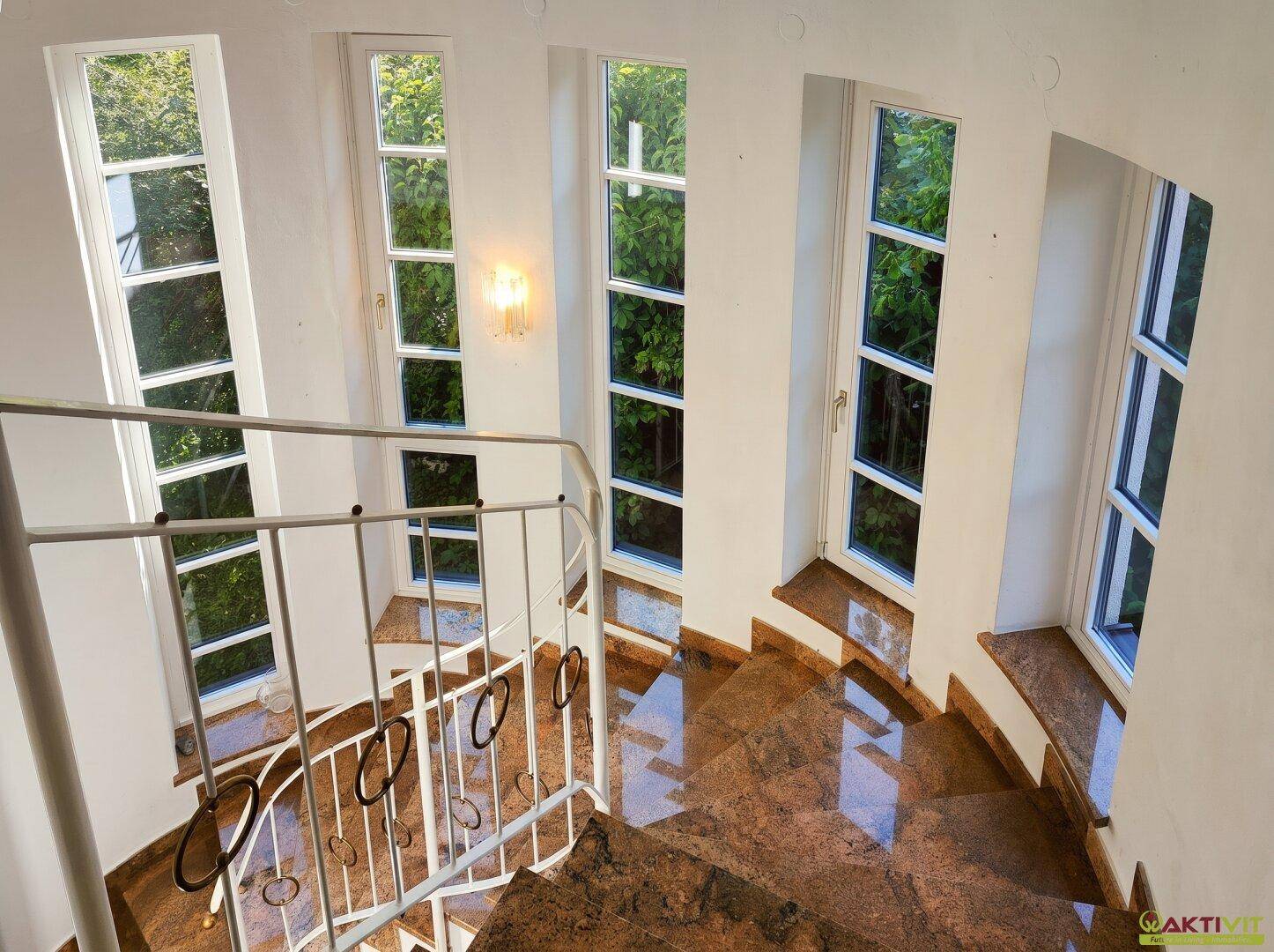 Elegante Wendeltreppe mit Granitstufen und hohen Fenstern, die viel Tageslicht hereinlassen.