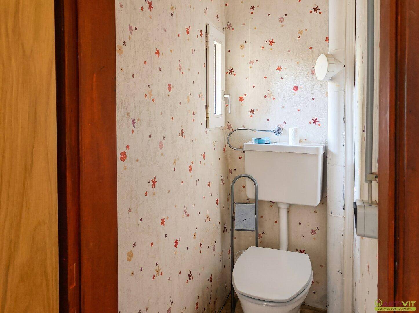 Kleines Gäste-WC mit floraler Tapete, Toilette und einem kleinen Fenster für Tageslicht.