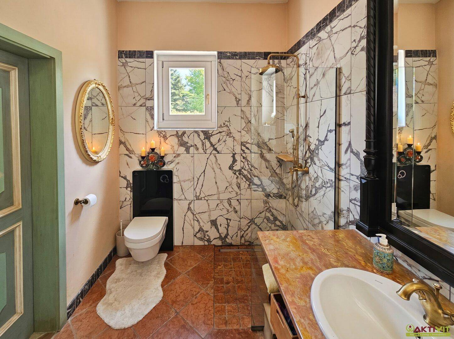 Marmoriertes Badezimmer mit Dusche, WC und Waschtisch mit Spiegel.