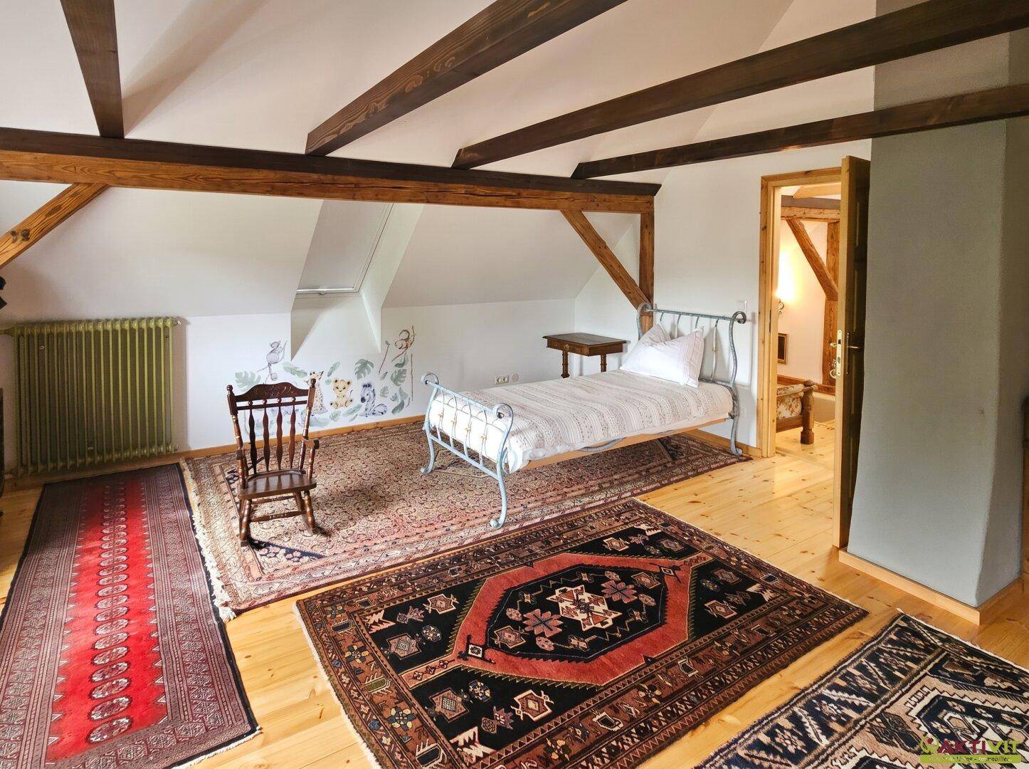 Geräumiges Schlafzimmer im Dachgeschoss mit Holzbalken und mehreren Teppichen.