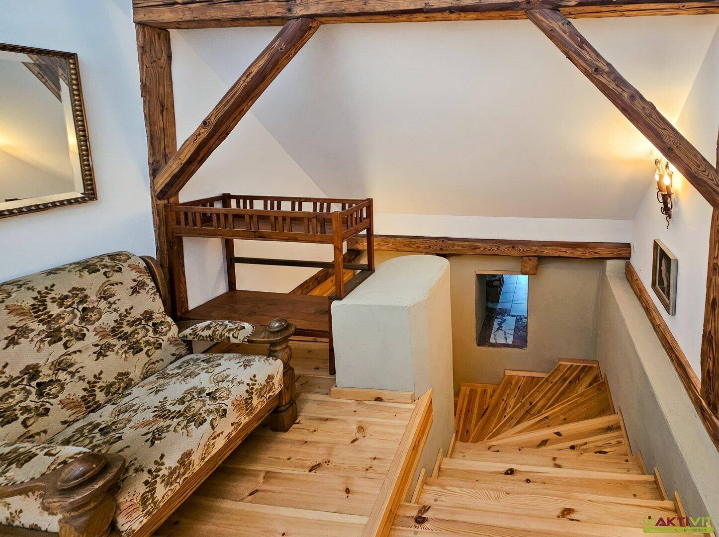 Holztreppe im Dachgeschoss mit rustikalen Holzbalken und Sitzbereich.