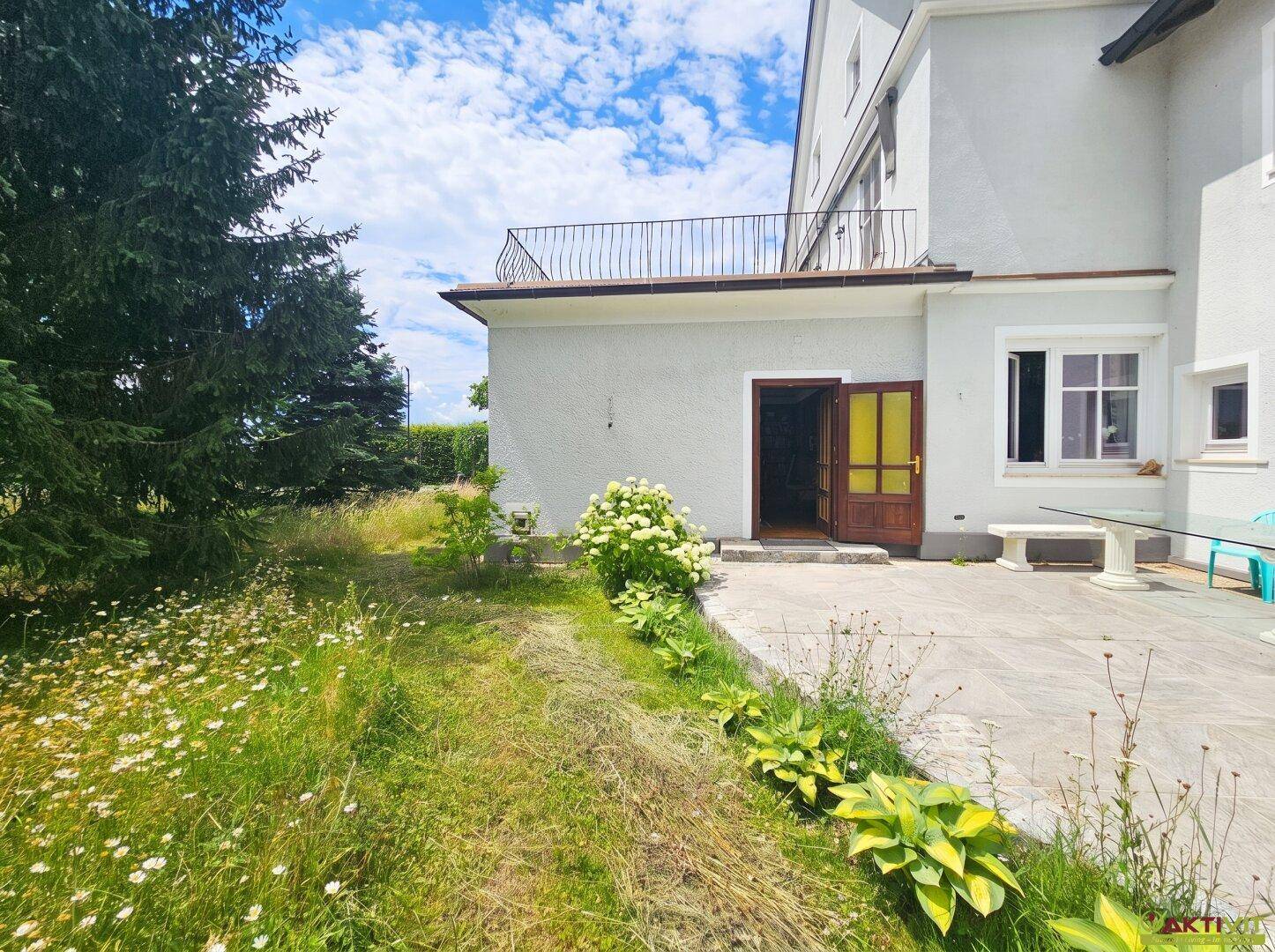 Großer Gartenbereich mit Terrasse, Rasen und üppiger Vegetation.