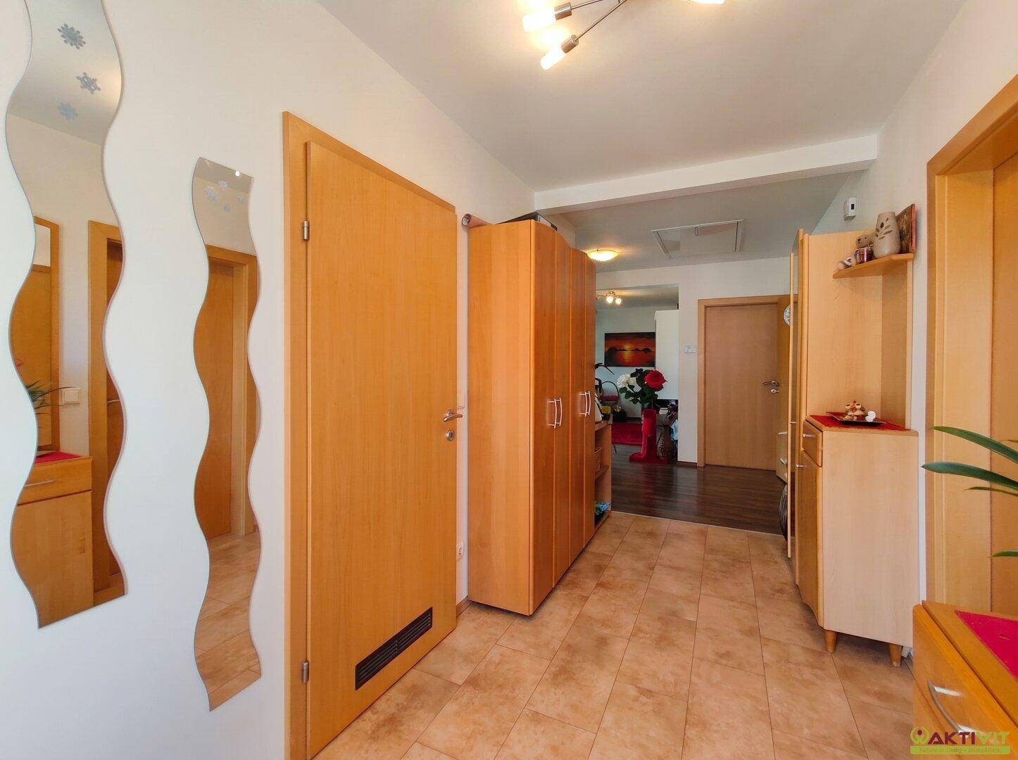 Heller Flur mit beigefarbenen Fliesen, Holzmöbeln und dekorativen Spiegeln an der Wand.