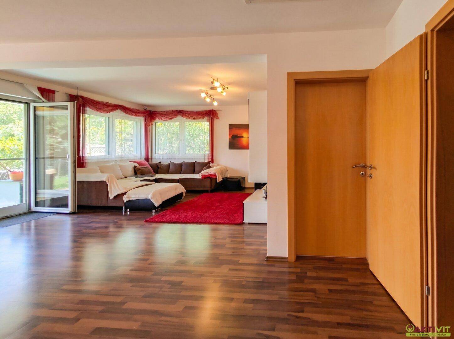 Geräumiges Wohnzimmer mit dunklem Laminatboden, rotem Teppich und Zugang zur Terrasse.