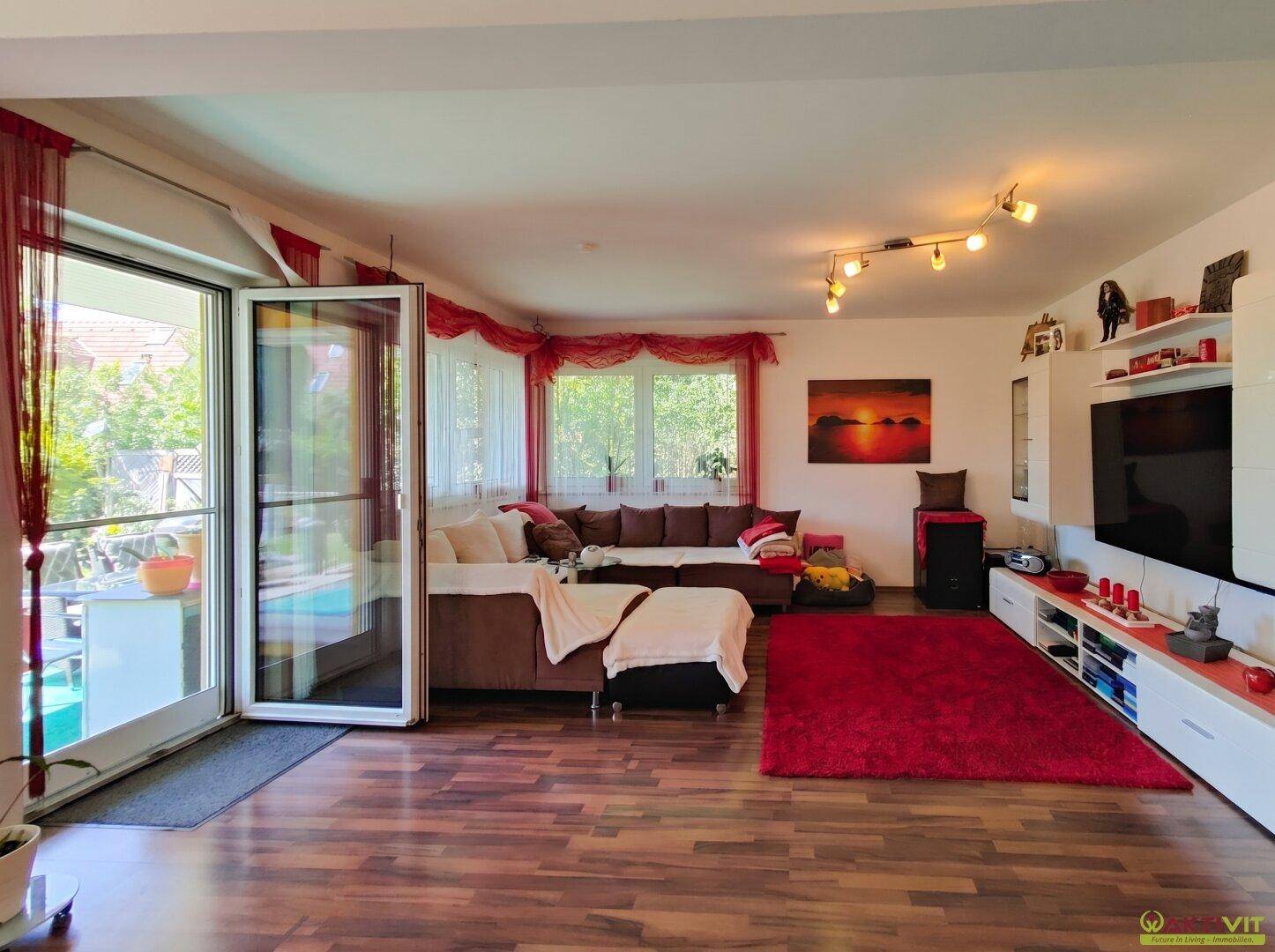 Helles Wohnzimmer mit großem Sofa, Medieneinheit und Blick in den Garten durch die Terrassentür.