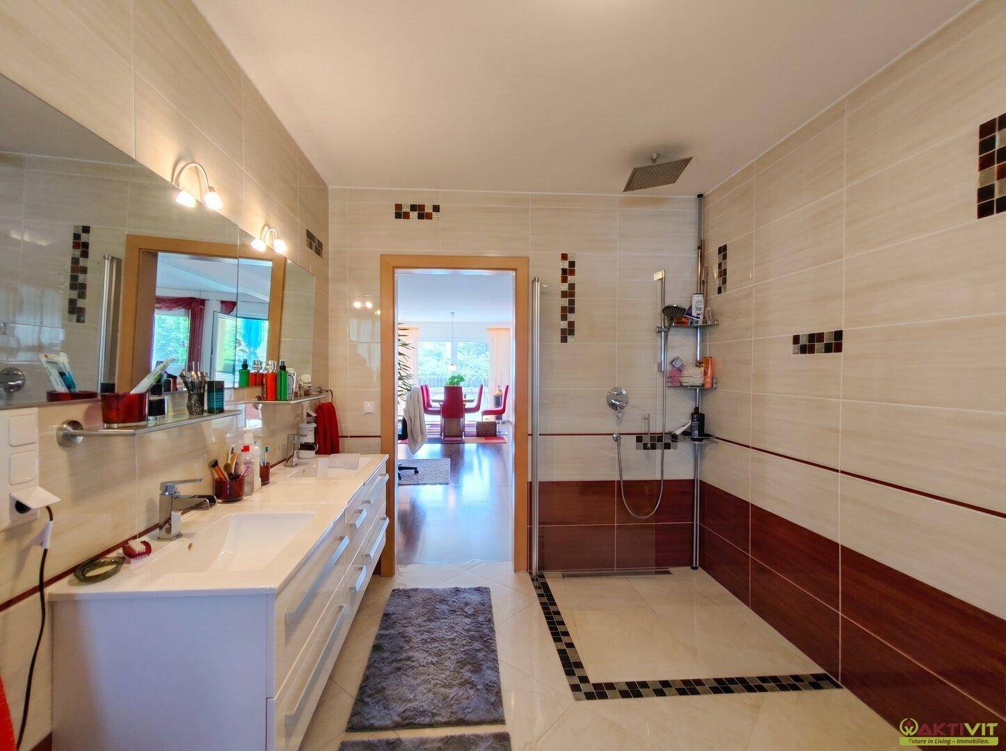 Modernes Badezimmer mit Doppelwaschbecken, begehbarer Dusche und Fliesen in Beige- und Brauntönen.