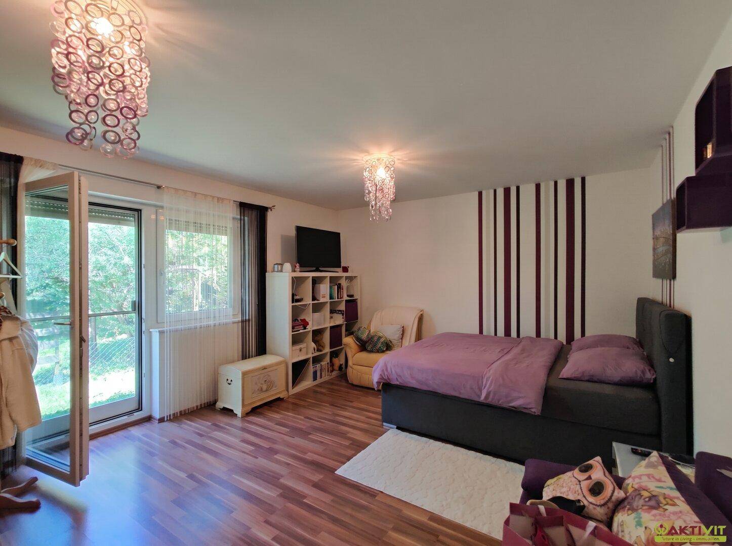 Schlafzimmer mit Holzboden, Doppelbett und Zugang zu einem Balkon oder einer Terrasse.
