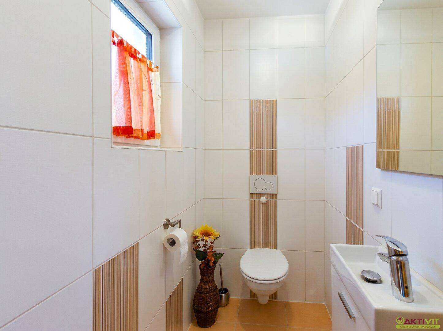 Kleines Gäste-WC mit Wand-WC, Waschbecken und Fenster, gefliest in Weiß und Beige.