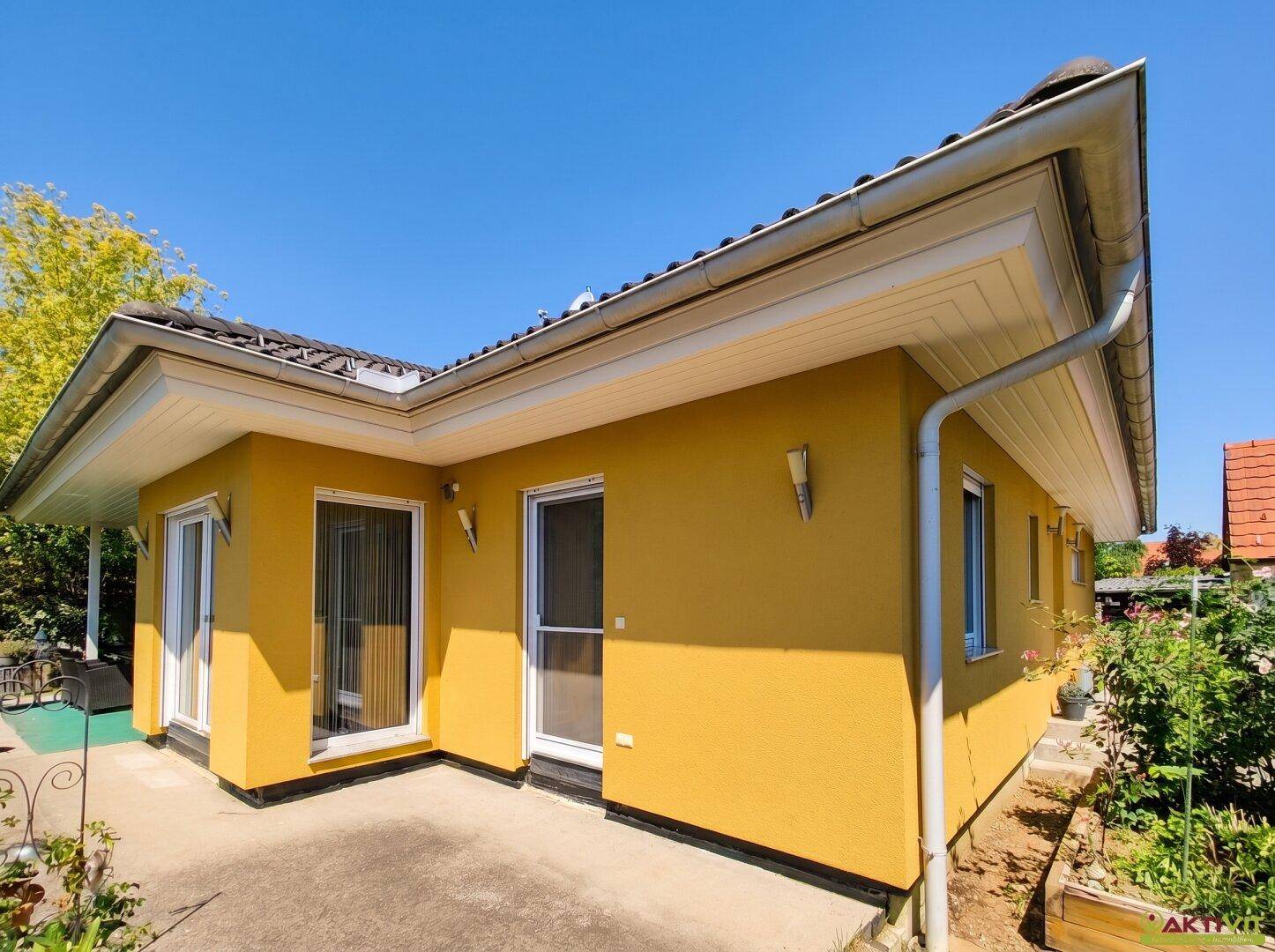 Seitenansicht des gelben Hauses mit Terrassentüren und einem kleinen gepflasterten Bereich.