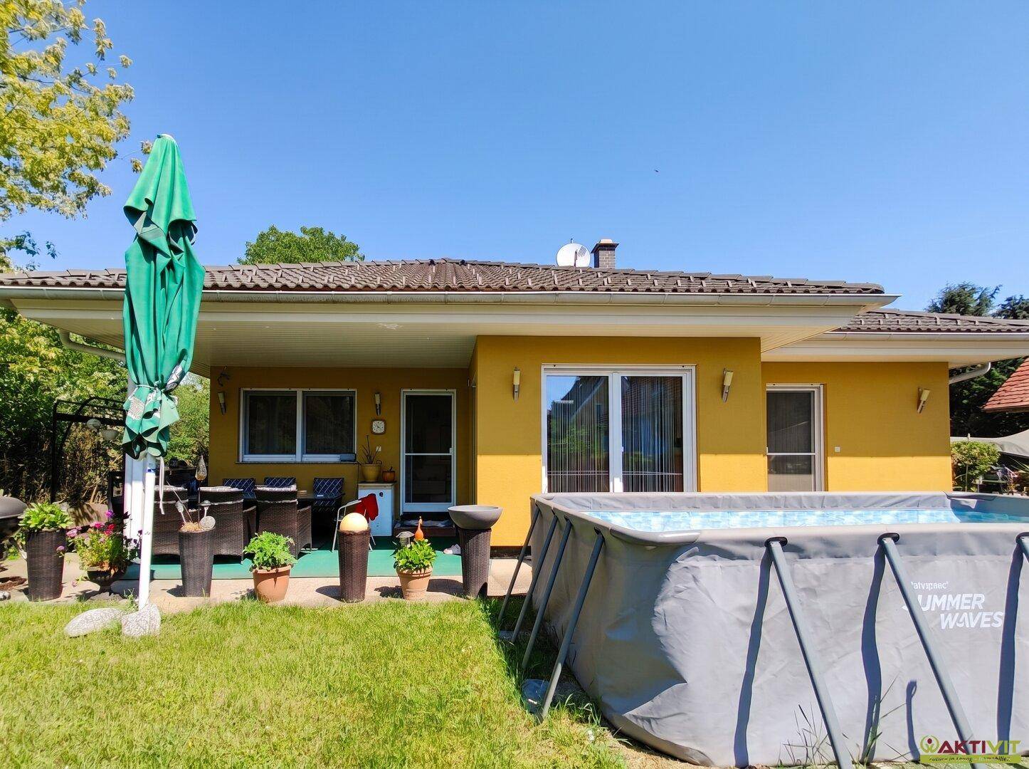 Rückansicht des Hauses mit Terrasse, Rasenfläche und einem aufgestellten Swimmingpool.