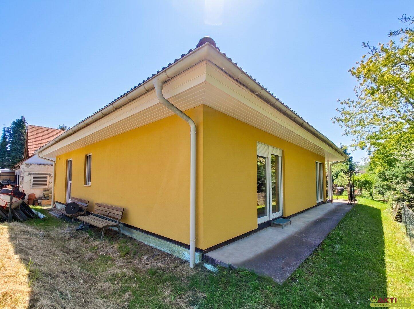 Seitenansicht des gelben Hauses mit grüner Rasenfläche und einigen Bäumen im Hintergrund.