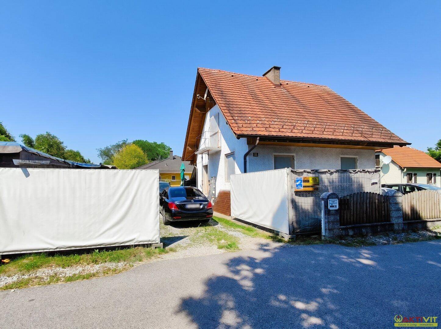 Älteres Gebäude mit Satteldach, Einfahrt und einem Zaun an der Straßenseite.